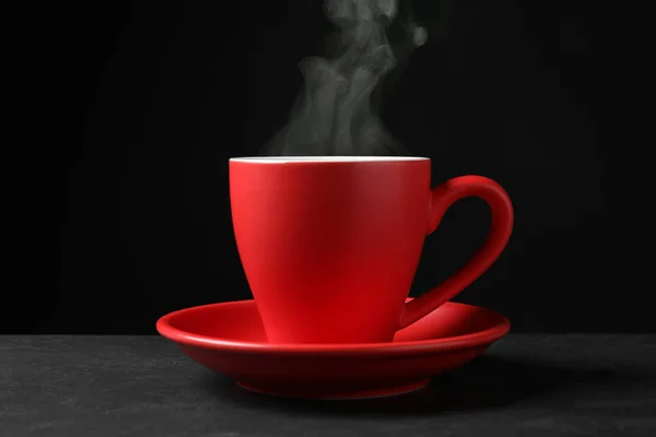 黒を背景にグレーテーブルの上に熱い蒸しコーヒーと赤カップ — ストック写真