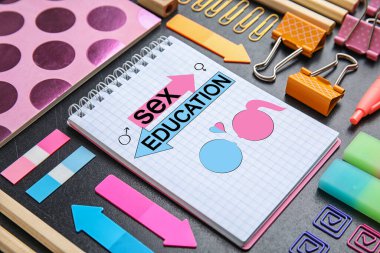 Not defterinde seks eğitimi, kalp, kadın ve erkek cinsiyet tabelaları, kadın ve erkek çizimleri ve masadaki diğer kırtasiyeler var.