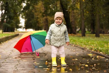 Cute little girl standing in puddle near colorful umbrella outdoors