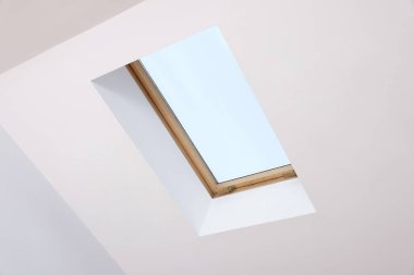 Skylight roof window and lamps on slanted ceiling in attic room, low angle view