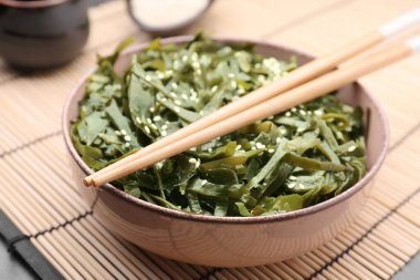 Fresh laminaria (kelp) seaweed in bowl and chopsticks on table, closeup