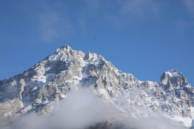 Picturesque landscape of high mountains covered with thick mist under blue sky