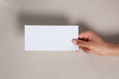 Man holding flyer on grey background, closeup. Mockup for design