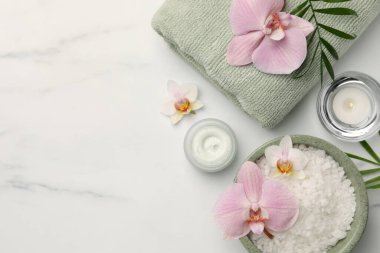 Flat lay composition with different spa products and flowers on white marble table. Space for text