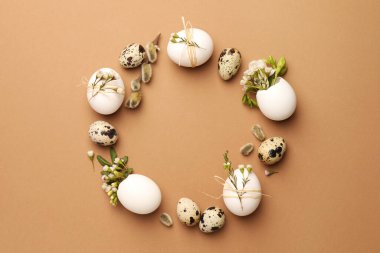 Frame made of eggs and natural decor on brown background, top view with space for text. Happy Easter