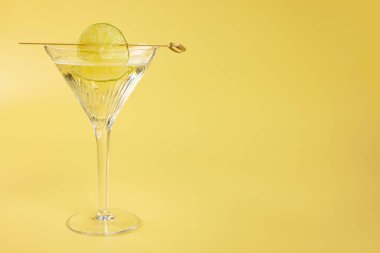 Sarı arka planda limon dilimli martini kokteyli, metin için boşluk