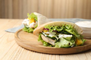 Delicious pita sandwiches with chicken breast and vegetables on wooden table, closeup