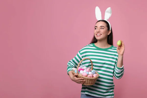 快乐的女人 戴着兔子耳朵的头巾 手里拿着一篮粉红色背景的彩绘复活节彩蛋 案文的篇幅 — 图库照片