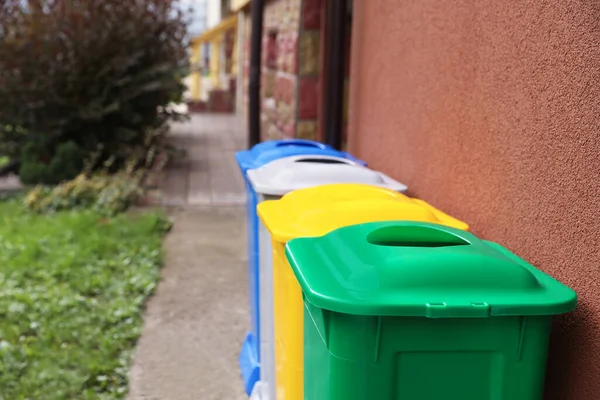 Many colorful recycling bins near brown wall outdoors
