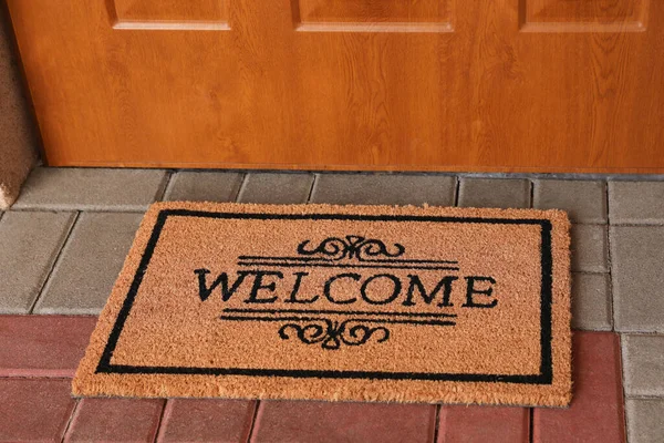 Door mat with word Welcome on street tiles near entrance