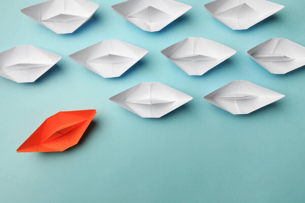 Orange paper boat floating away from others on light background, flat lay. Uniqueness concept