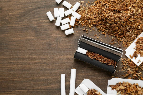 stock image Flat lay composition with roller and tobacco on wooden table, space for text. Making hand rolled cigarettes