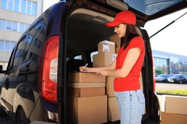 Courier with clipboard checking packages near delivery van outdoors
