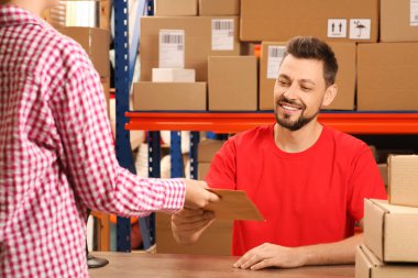 Kadın postanedeki işçiden paket alıyor.