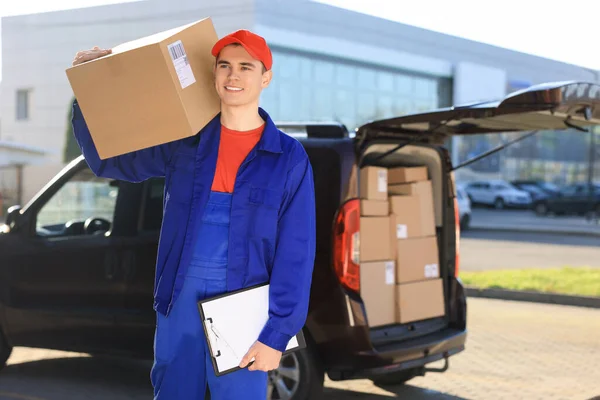 Courier with parcel and clipboard near delivery van outdoors