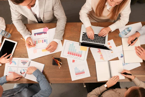 Team of employees working together at wooden table in office, above view