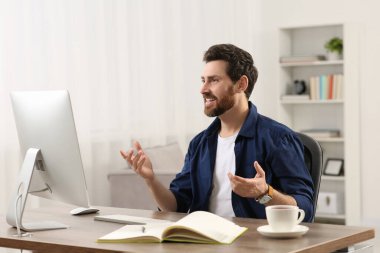 Ev işyerinde. Odanın ahşap masasında video konferansı yapan mutlu adam.