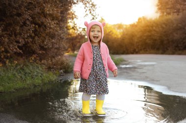 Little girl wearing rubber boots walking in puddle outdoors
