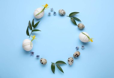 Şenlikli Paskalya yumurtaları, yeşil yapraklar ve çiçeklerin çerçevesi açık mavi arka plan, üst manzara. Metin için boşluk