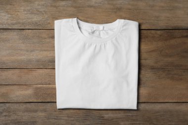 Stylish white T-shirt on wooden table, top view