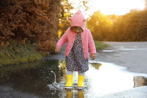 小さな女の子身に着けていますゴムブーツ歩くで水たまり屋外 — ストック写真
