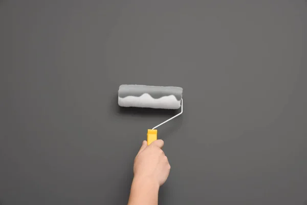 Worker using roller to paint wall with grey dye, closeup