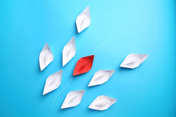 Red paper boat floating between others on light blue background, flat lay. Uniqueness concept