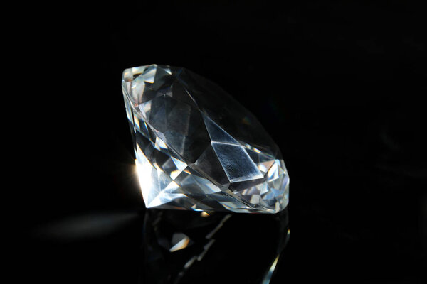 Beautiful dazzling diamond on black mirror background, closeup