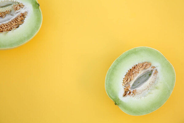 Halves of fresh ripe honeydew melon on yellow background, flat lay. Space for text