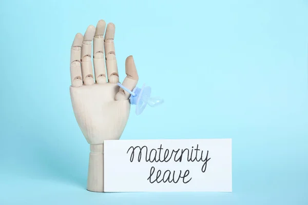 Wooden mannequin hand, pacifier and card with phrase Maternity Leave on light blue background. Space for text