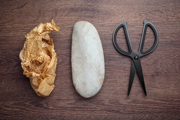 Rock, crumpled paper and scissors on wooden table, flat lay