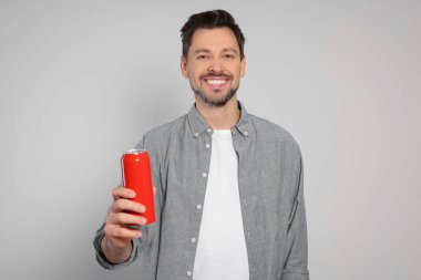 Happy man holding red tin can with beverage on light grey background