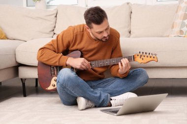 Evde online müzik kursuyla gitar çalmayı öğrenen bir adam. Hobi zamanı.