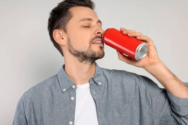 赤い錫を飲む幸せな男はライトグレーの背景に缶 — ストック写真
