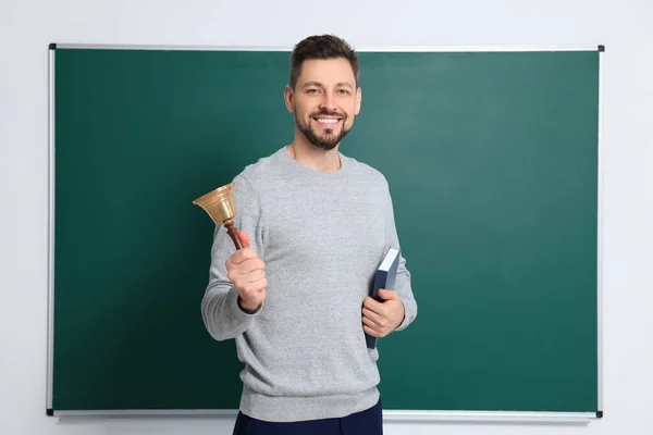 Teacher with school bell near chalkboard indoors. Space for text