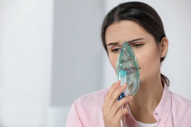 Sick young woman using nebulizer at home, space for text