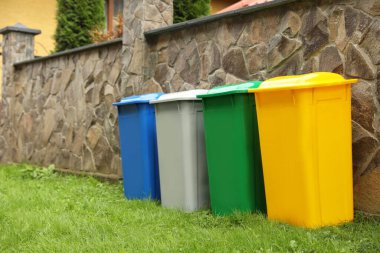 Dışarıda taş çitlerin yanında renkli geri dönüşüm kutuları var.