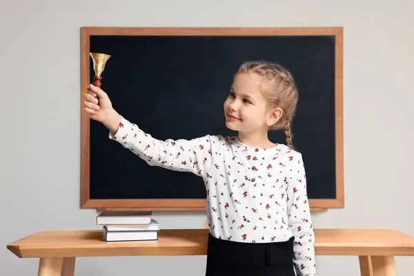 Pupil with school bell near desk and chalkboard in classroom