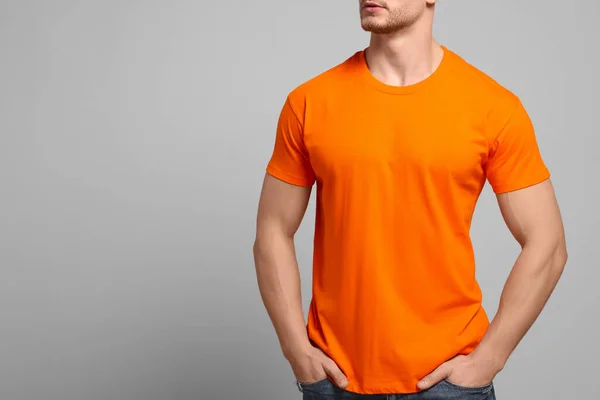Man wearing orange t-shirt on light grey background, closeup. Mockup for design