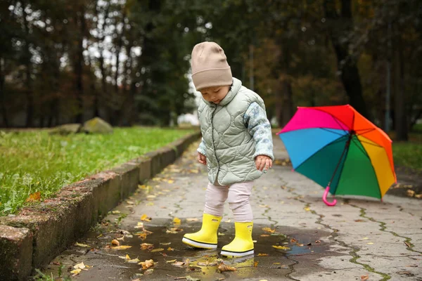 可爱的小女孩走在外面五彩缤纷的雨伞旁的水坑里 — 图库照片