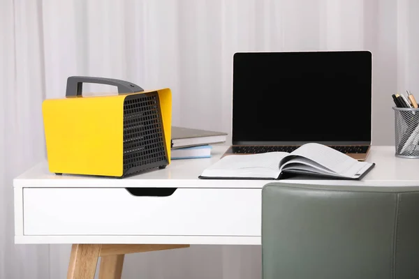 Modern electric fan heater near laptop and notebooks on white table in office