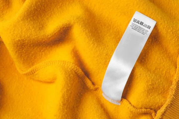 Clothing label with care recommendations on orange garment, top view. Space for text