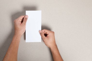 Man holding flyer on grey background, closeup. Mockup for design