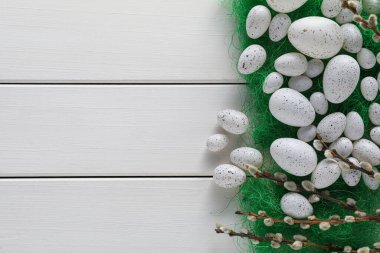 Many beautifully painted Easter eggs and pussy willow branches on white wooden table, flat lay. Space for text