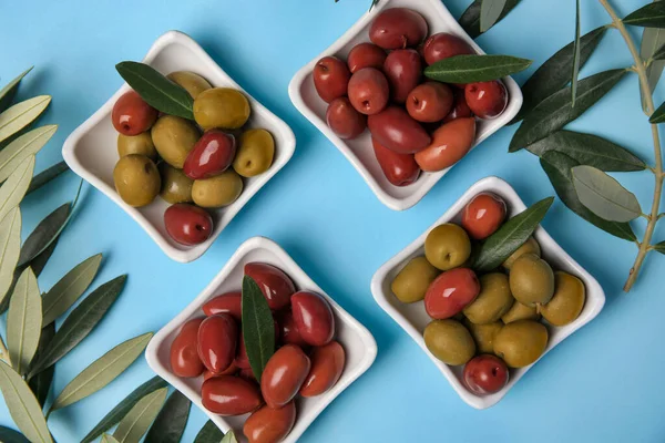 Different fresh olives and green leaves on light blue background, flat lay