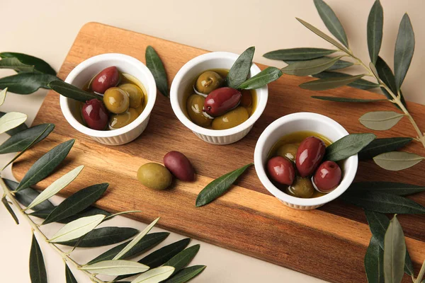 Bowls with different ripe olives and leaves on beige background
