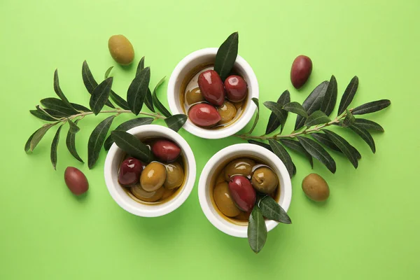 Bowls with different ripe olives and leaves on light green background, flat lay