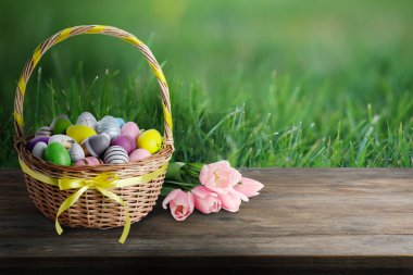 Şenlikli Paskalya yumurtaları ve yeşil çayır üzerinde ahşap masa laleleri ile hasır sepet, metin için yer