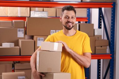 Post office worker with parcels near rack indoors