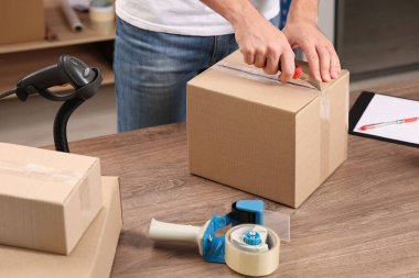 Post office worker with utility knife opening parcel at counter indoors, closeup